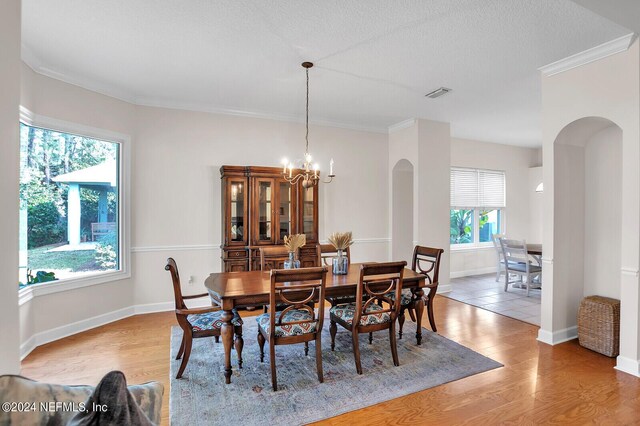 dining space featuring crown molding, a chandelier, a textured ceiling, and light hardwood / wood-style flooring