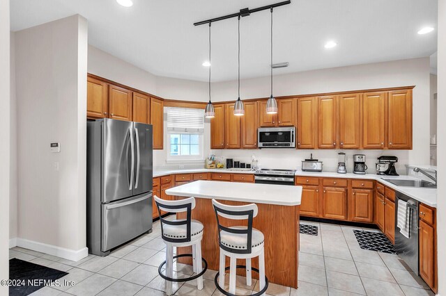 kitchen with appliances with stainless steel finishes, a breakfast bar, sink, hanging light fixtures, and a kitchen island