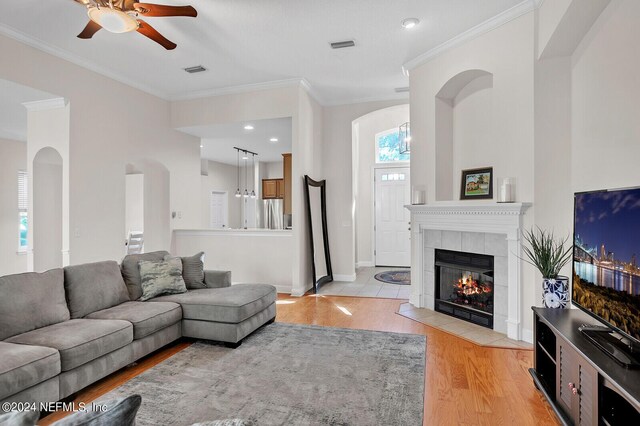 living room featuring a tile fireplace, ceiling fan, light wood-type flooring, and crown molding