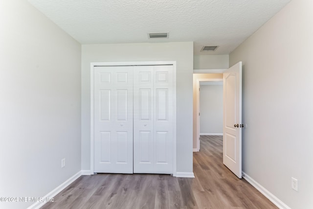 unfurnished bedroom with light hardwood / wood-style floors, a textured ceiling, and a closet