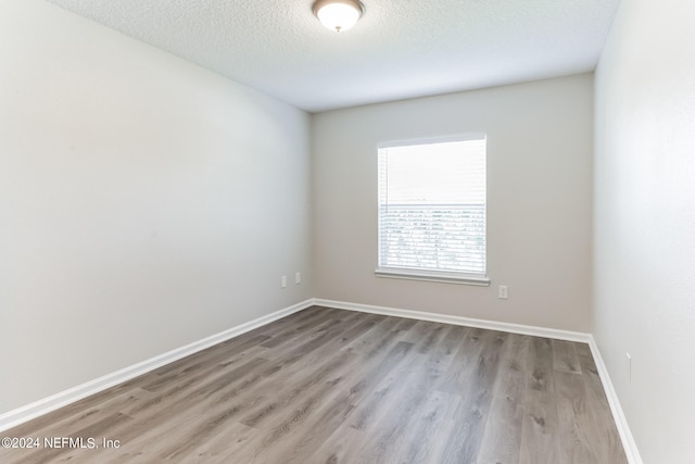 empty room with a textured ceiling and light hardwood / wood-style flooring