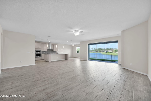 unfurnished living room featuring ceiling fan, a textured ceiling, and light wood-type flooring