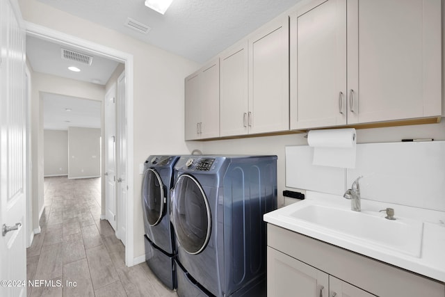 clothes washing area with cabinets, sink, light hardwood / wood-style flooring, washing machine and dryer, and a textured ceiling