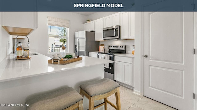 kitchen featuring light tile patterned flooring, a breakfast bar, white cabinets, kitchen peninsula, and stainless steel appliances