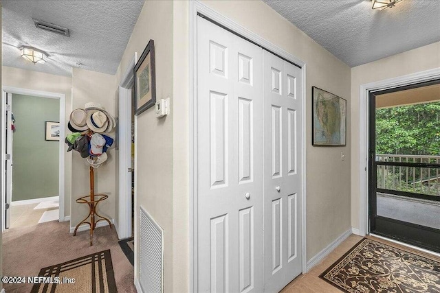 foyer featuring light carpet, visible vents, and a textured ceiling