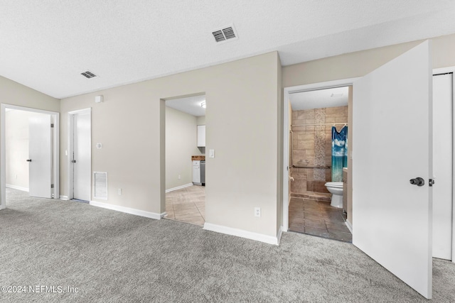 unfurnished bedroom featuring ensuite bath, light carpet, a closet, and a textured ceiling