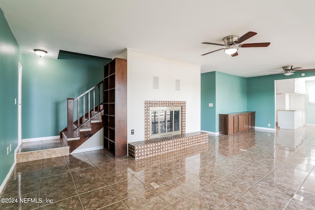 unfurnished living room featuring a tiled fireplace, ceiling fan, and tile patterned flooring