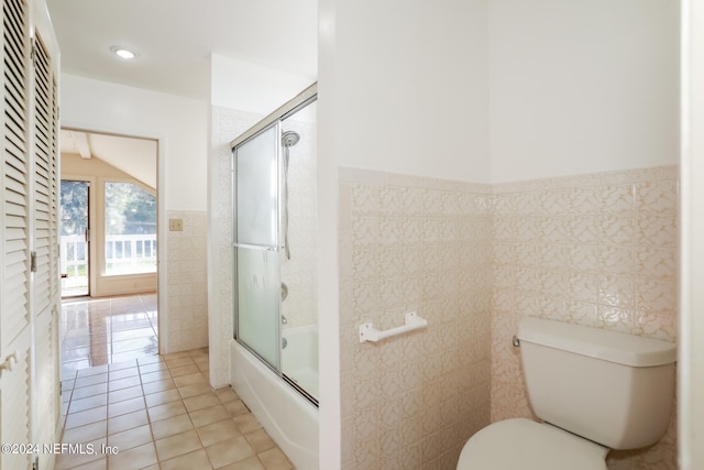 bathroom with tile patterned flooring, tile walls, combined bath / shower with glass door, and toilet