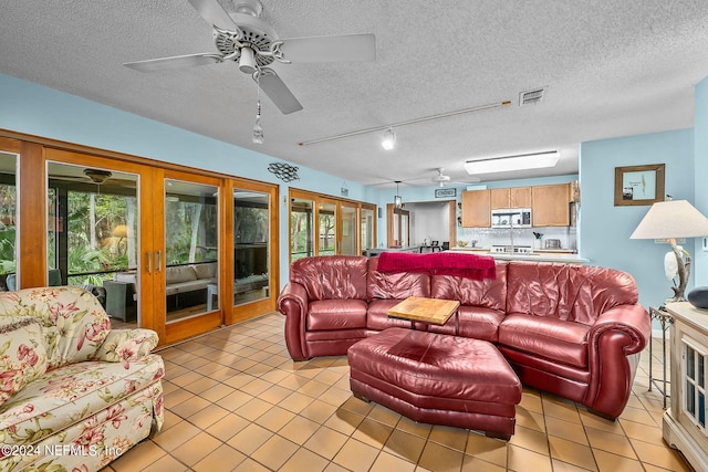 living room with ceiling fan, rail lighting, light tile patterned floors, and a textured ceiling