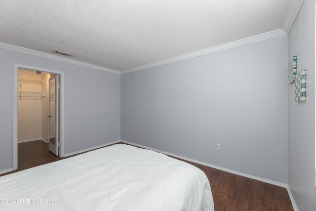 bedroom with crown molding, dark wood-type flooring, a textured ceiling, a spacious closet, and a closet