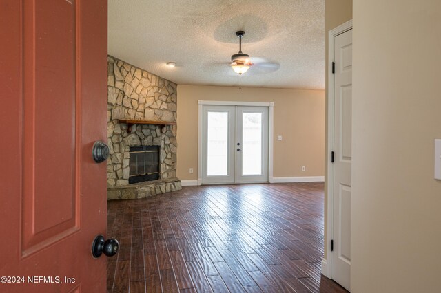 unfurnished living room featuring a fireplace, french doors, a textured ceiling, dark wood-type flooring, and ceiling fan