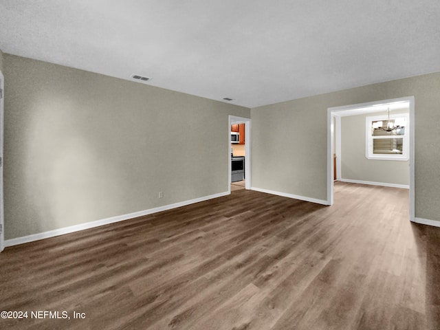 spare room with dark wood-type flooring and an inviting chandelier