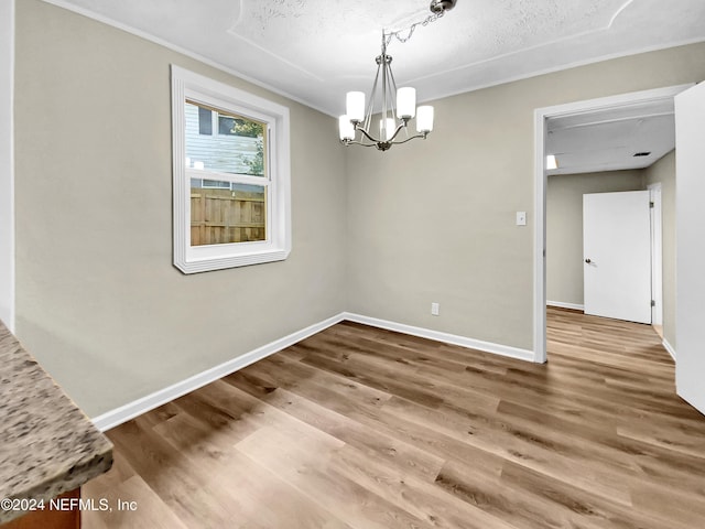 unfurnished dining area with an inviting chandelier, wood-type flooring, and a textured ceiling