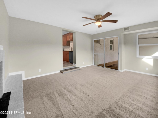 unfurnished living room with a fireplace, ceiling fan, sink, and carpet floors