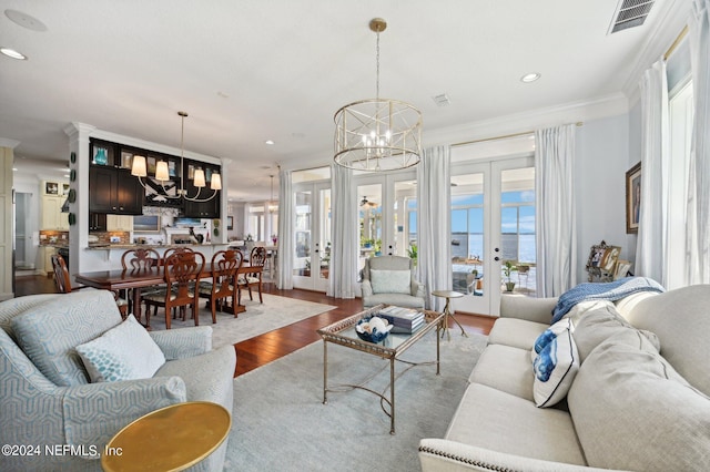 living room with french doors, a water view, visible vents, wood finished floors, and a chandelier