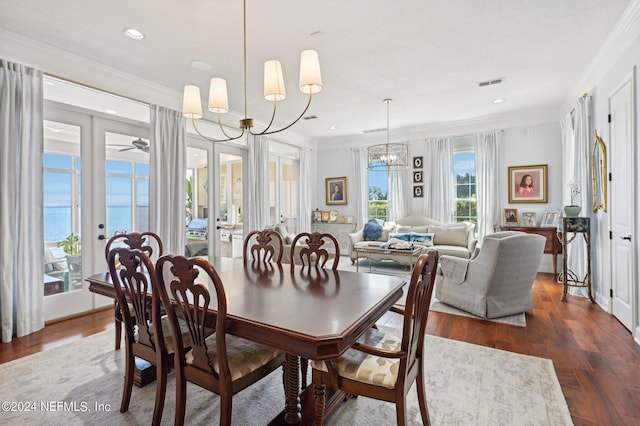 dining room with visible vents, dark wood finished floors, ornamental molding, a water view, and a chandelier