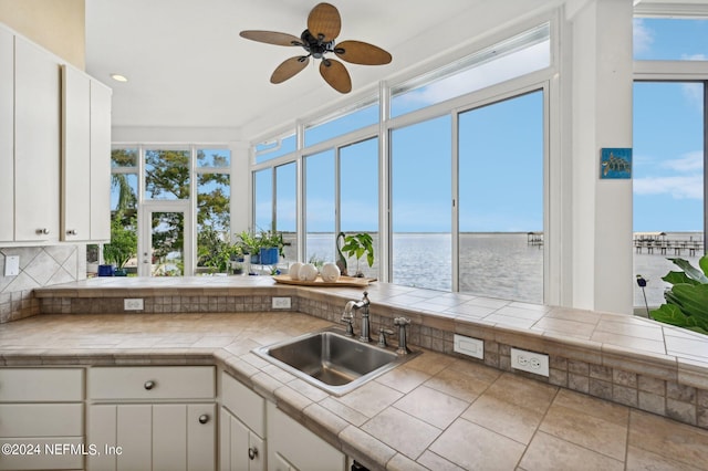 kitchen with tile countertops, a water view, a sink, white cabinetry, and a wealth of natural light