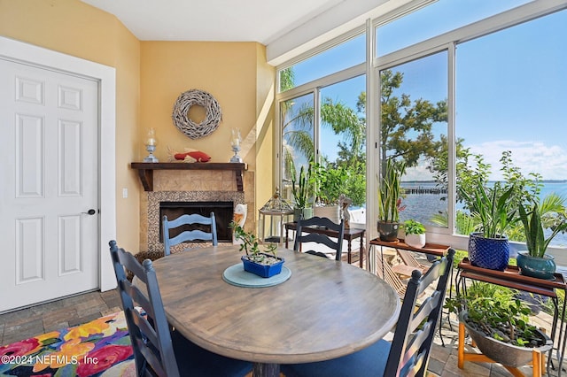 dining space with stone tile flooring, a water view, and a tiled fireplace