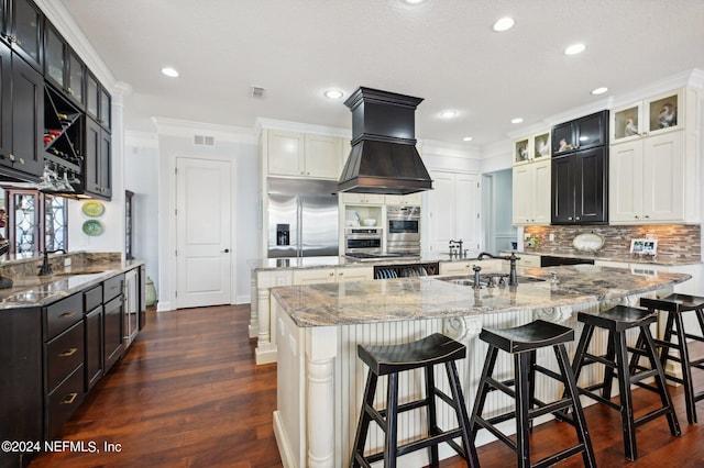 kitchen with a center island with sink, glass insert cabinets, island range hood, built in refrigerator, and a kitchen breakfast bar