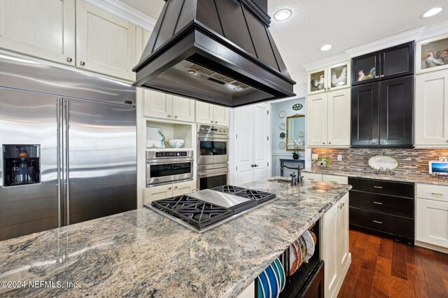 kitchen featuring stainless steel appliances, glass insert cabinets, light stone counters, and island range hood