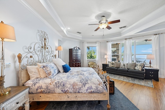 bedroom featuring light wood-type flooring, a tray ceiling, visible vents, and crown molding