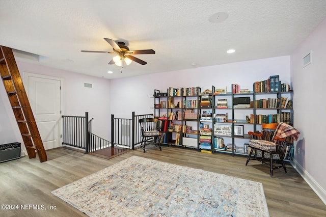 sitting room with a textured ceiling, wood finished floors, visible vents, an upstairs landing, and baseboards