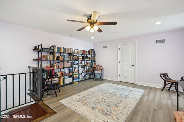 sitting room with a textured ceiling, wood finished floors, visible vents, and baseboards