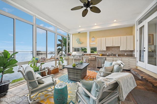 sunroom / solarium featuring a ceiling fan, french doors, a water view, and a sink