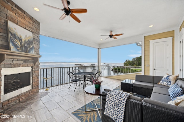 view of patio / terrace with a water view, an outdoor living space with a fireplace, a ceiling fan, and outdoor dining space