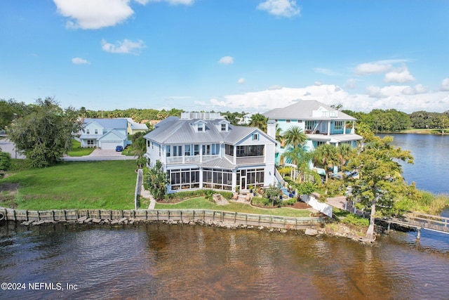 back of house with a water view, a sunroom, and a lawn