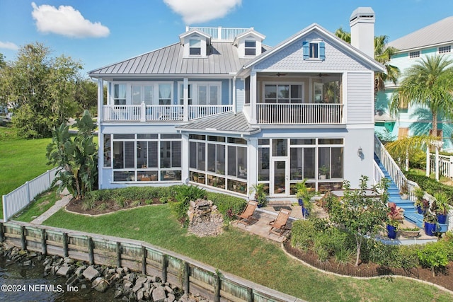 rear view of property with a sunroom, a chimney, a standing seam roof, fence, and a yard