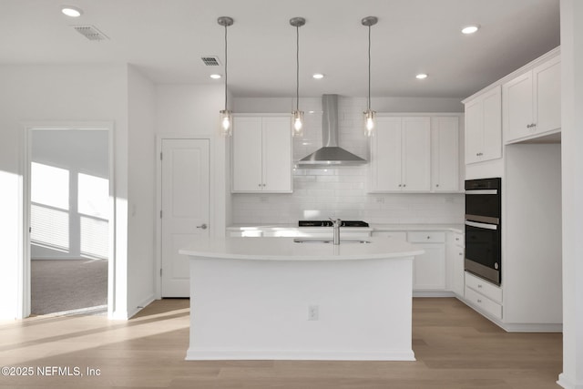 kitchen featuring white cabinets, a kitchen island with sink, and wall chimney range hood