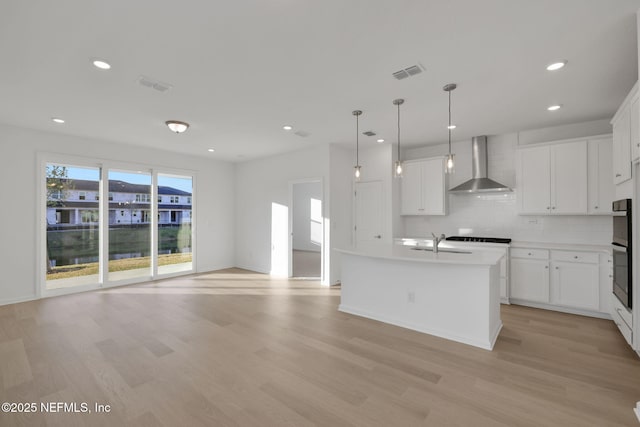 kitchen with pendant lighting, wall chimney range hood, a kitchen island with sink, and white cabinets