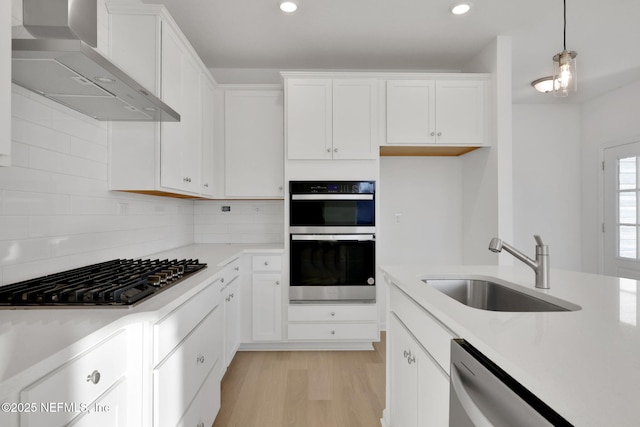 kitchen featuring white cabinets, decorative light fixtures, sink, and wall chimney range hood