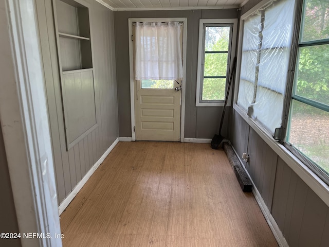 doorway with baseboards, wooden walls, built in features, and light wood-style floors