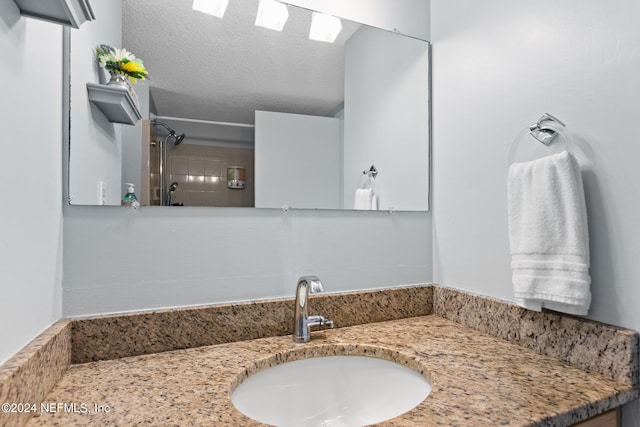 bathroom with a textured ceiling, vanity, and walk in shower