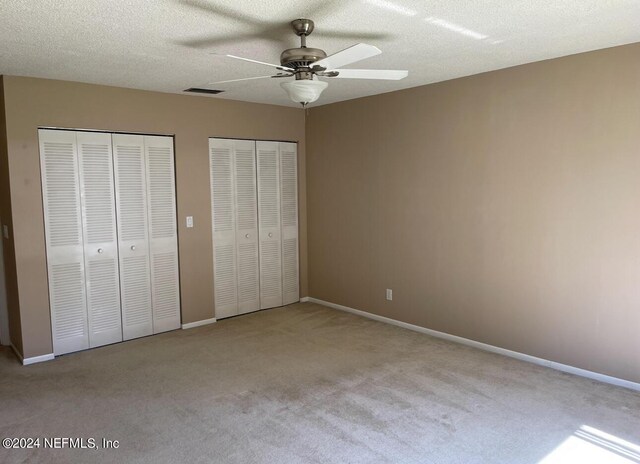 unfurnished bedroom with multiple closets, carpet flooring, a textured ceiling, and ceiling fan