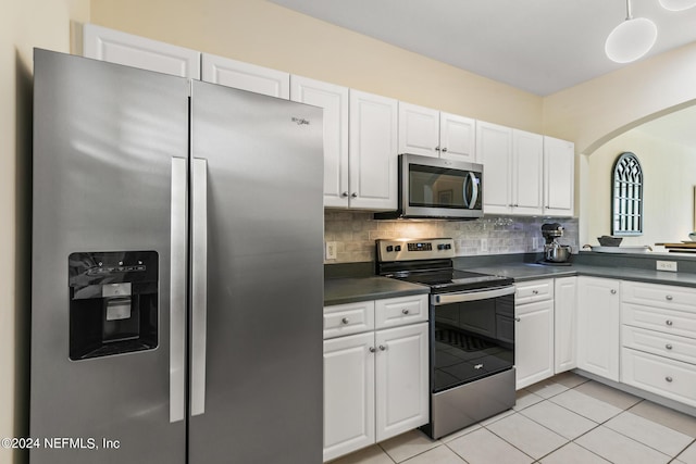 kitchen with light tile patterned floors, dark countertops, decorative backsplash, appliances with stainless steel finishes, and white cabinetry