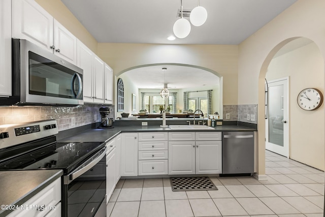 kitchen with white cabinets, dark countertops, stainless steel appliances, pendant lighting, and a sink