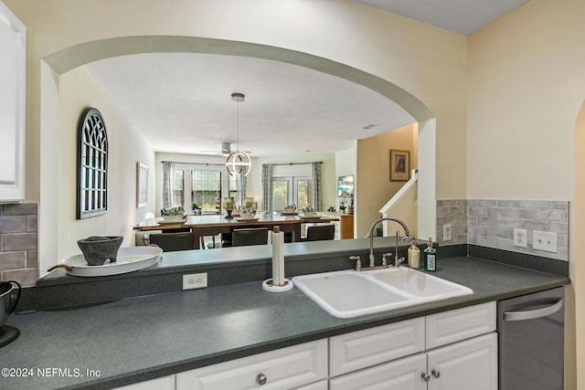 kitchen featuring decorative backsplash, dishwasher, white cabinets, dark countertops, and a sink