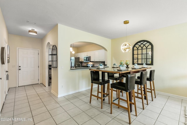 dining space with light tile patterned floors, arched walkways, visible vents, and baseboards