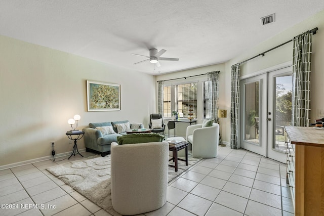 living area with light tile patterned floors, visible vents, a ceiling fan, a textured ceiling, and baseboards