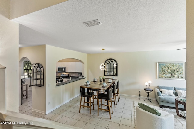 dining area with light tile patterned floors, baseboards, visible vents, arched walkways, and a textured ceiling