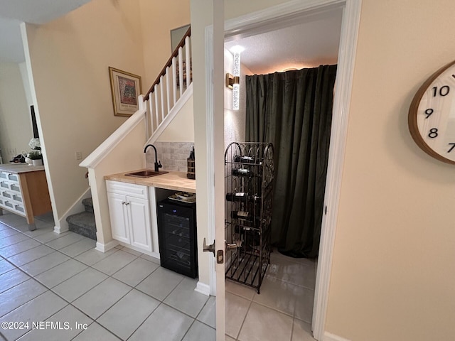 bar featuring light tile patterned floors, beverage cooler, decorative backsplash, stairway, and a sink