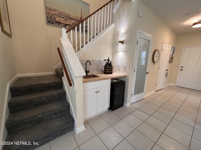 bar with sink, white cabinetry, tasteful backsplash, light tile patterned floors, and beverage cooler