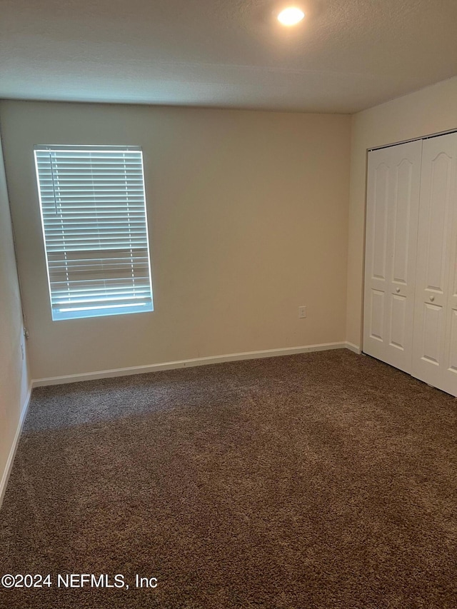 unfurnished bedroom featuring baseboards, dark colored carpet, and a closet