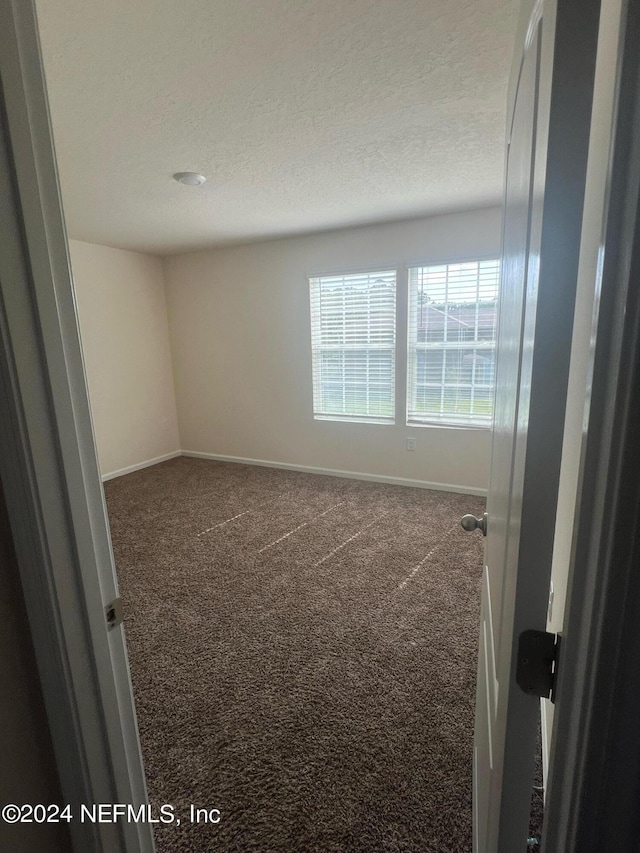 spare room featuring a textured ceiling, dark colored carpet, and baseboards