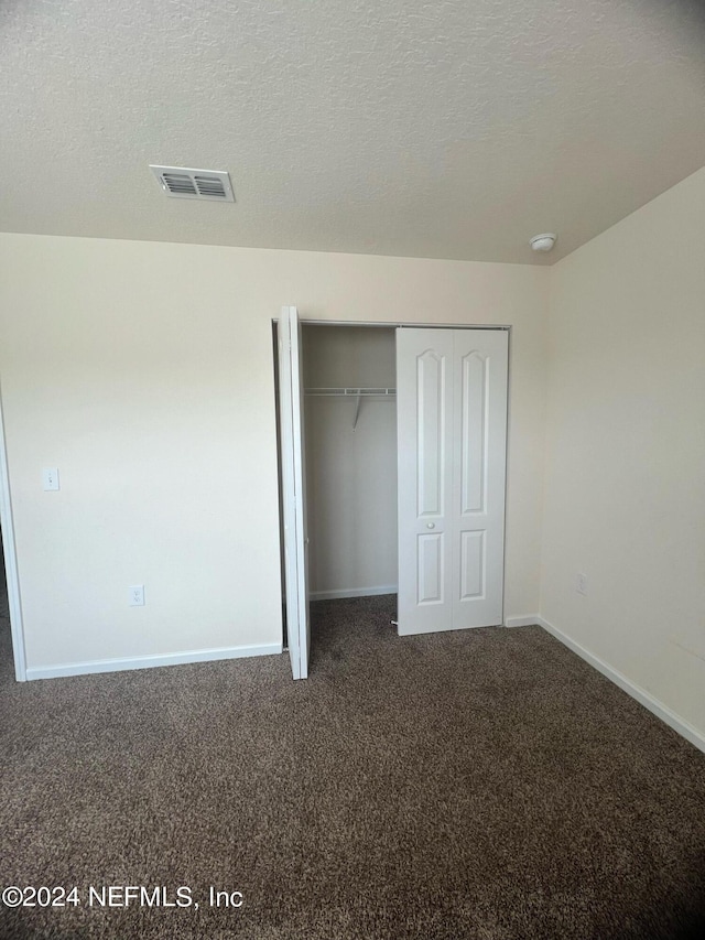 unfurnished bedroom with a textured ceiling, visible vents, baseboards, a closet, and dark carpet