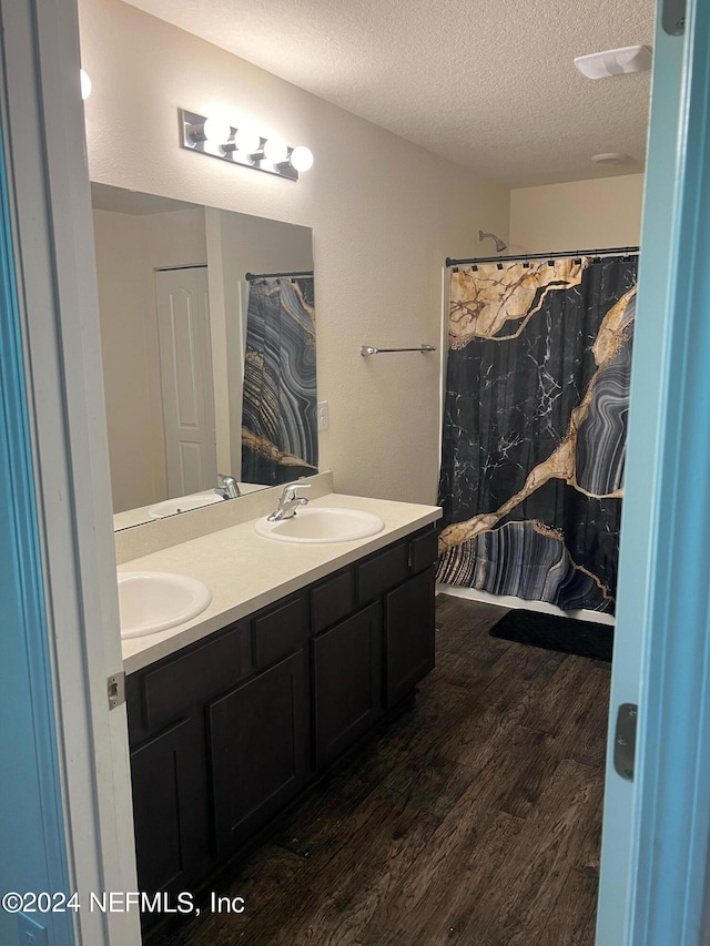 full bathroom featuring double vanity, a textured ceiling, a sink, and wood finished floors