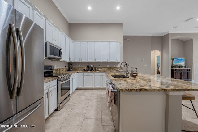 kitchen with light stone countertops, sink, stainless steel appliances, white cabinets, and a center island with sink